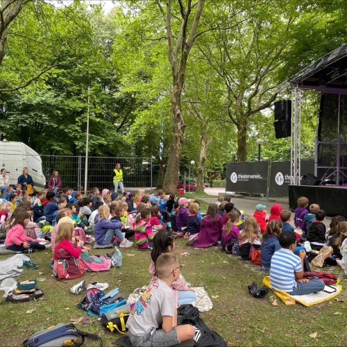 Kinder sitzen im Gras vor der Theaterbühne