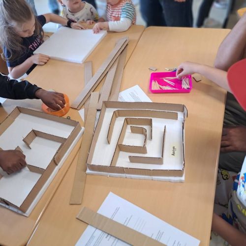 Kinder, die an einem Tisch eigene Murmelbahnen aus Pappe bauen