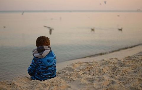 Kind sitzt im Sand und schaut aufs Wasser